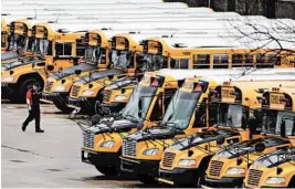  ?? CHARLES KRUPA/AP ?? A worker passes long-idled school buses parked at a depot in Manchester, New Hampshire, as public school children continue to be taught with remote learning.