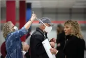  ??  ?? Poll worker Patty Piek-Groth, left, helps fellow poll worker Jerry Moore, center, put on a mask to prevent the spread of coronaviru­s as the polls open for the primary election.