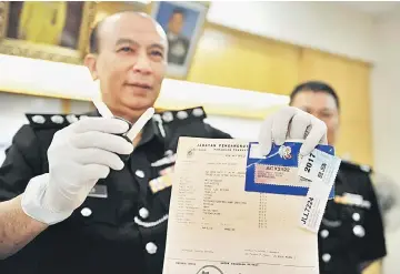  ??  ?? Rosly showing a blank key, fake road tax and green card seized during the press conference in Putrajaya. — Bernama photo