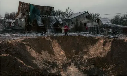  ?? ROMAN PILIPEY/AFP VIA GETTY IMAGES ?? A communal worker walked next to a crater and destroyed houses after a Russian shelling in Kyiv, on Dec. 11.