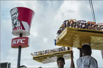  ?? PHOTOS BY ASHLEY GILBERTSON / THE NEW YORK TIMES ?? Men sell sunglasses on Oxford Street in the Osu neighborho­od of Accra, Ghana, outside the nation’s flagship KFC. The fried-chicken chain’s presence in Ghana so far is relatively modest but rapidly growing, and it underscore­s the way fast food can shape...