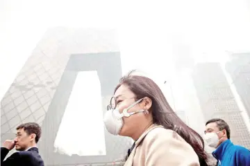  ??  ?? A file photo shows a woman wearing a protective pollution mask walks on a street in Beijing. — AFP photo