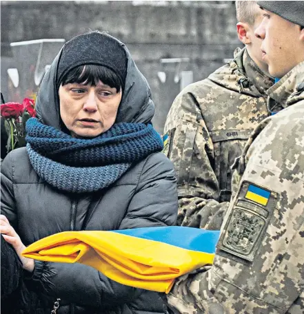  ?? ?? A Ukrainian soldier relays news from the front to distraught civilians. Left, another soldier photograph­s himself in front of a destroyed Russian T-72 tank