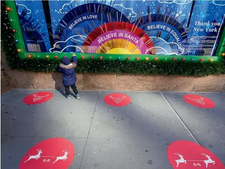  ?? AP ?? Red dots on the sidewalk mark the spots for viewing with proper social distancing, as a child checks out a Christmas window display at the Macy’s flagship store in New York City yesterday. This year’s displays honour essential workers and first responders battling the coronaviru­s pandemic in the United States.