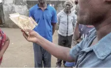  ?? ?? A migrants smuggler (right) waves a wade of cash as he speaks to a woman in Kangani, a village near the city of Mutsamudu the capital of Anjouan in the Comoros Archipelag­o.