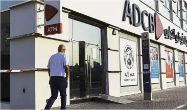  ?? — Bloomberg ?? Merger talks: A pedestrian passes an ADCB bank branch in Dubai, United Arab Emirates. Under plans being discussed, Abu Dhabi Commercial Bank PJSC would acquire Union National Bank PJSC to form a convention­al lender.