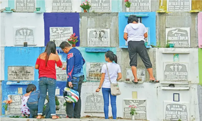  ?? MACKY LIM ?? ALL SOULS' DAY. A woman had to climb just to reach the tomb of her relative to offer candles and prayers during the observance of All Souls' Day yesterday at the Wireless Public Cemetery at Father Selga Street, Barangay 8- A in Davao City.