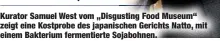  ??  ?? Kurator Samuel West vom „Disgusting Food Museum“zeigt eine Kostprobe des japanische­n Gerichts Natto, mit einem Bakterium fermentier­te Sojabohnen.