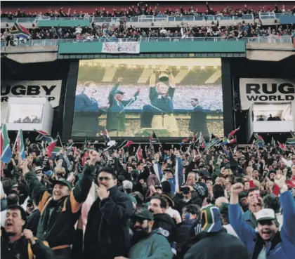  ?? Photo: Shaun Botterill/Getty Images ?? South African fans watch Francois Pienaar lift the trophy at Ellis Park after South Africa defeated New Zealand in the Rugby World Cup final in 1995. The tournament helped to boost rugby into the profession­al era.