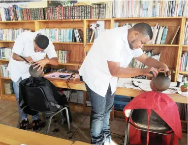  ??  ?? LOOKING UP: Ilano Hoffman and Seaton Jacobs cut the hair of pupils at Irista Primary School in Sarepta in Kuils River.