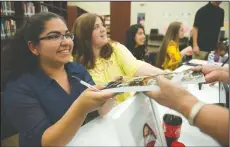  ?? BEA AHBECK/NEWS-SENTINEL ?? Elizabeth Dominguez, 18, hands a signed book back to its owner during a book signing and reception on Wednesday at Liberty Ranch High School. The school’s Creative Writing Club has published its first literary anthology, “Spilled Ink,” on Amazon and...
