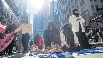  ?? AP ?? Women pray as two men check a flag during a rally in support of Muslim Americans and protest against President Donald Trump’s immigratio­n policies in Times Square, New York, on Sunday.