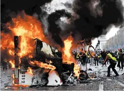  ?? BERTRAND GUAY/GETTY-AFP ?? A man throws a bike in a burning truck during a protest against rising oil prices and living costs near the Arc de Triomphe on the Champs-Elysees in Paris on Saturday.