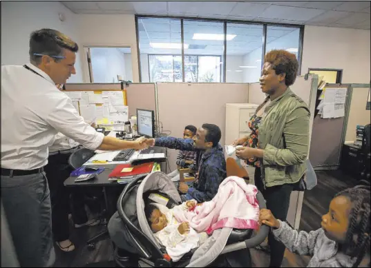  ?? Gregory Bull The Associated Press ?? Chris Williams, left, of Catholic Charities, shakes hands with a father from Nigeria during a visit at the agency’s San Diego affiliate July 17. Some local Catholic Charities affiliates are reporting a decline in donations.