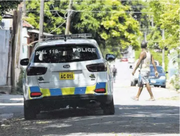  ?? (Photo: Joseph Wellington) ?? A resident of Southside in Central Kingston walks past a mobile police patrol team in the community yesterday following a fresh flare-up of violence in the area.