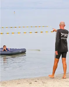  ??  ?? A lifeguard watches as children swim in the Sea of Galilee near Kibbutz Ein-Gev.