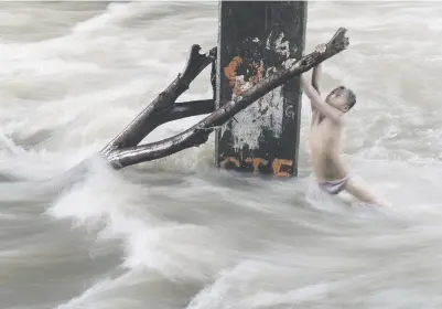  ?? Picture: AFP ?? A boy holds a partially submerged branch as he plays in a swollen river caused by heavy rains under a bridge in Manila yesterday.