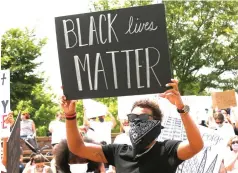  ?? Sue Ogrocki/Associated Press ?? ■ Atlanta Hawks guard Trae Young holds a "Black Lives Matter" sign during a peaceful rally on June 1 in his hometown of Norman, Okla., calling attention to the killing of George Floyd. While NBA players are using the season restart to demand change; coaches in the league are not making them walk down that path alone.