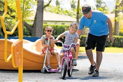  ?? AMY BETH BENNETT/SOUTH FLORIDA SUN SENTINEL ?? Chad Racine, of Fort Lauderdale, steadies his daughter, Aura, 4, as she learns to ride her bicycle at Bayview Park in Fort Lauderdale on Wednesday. Aura’s sister, Linda, 6, cheers her on. South Florida is headed for a warmer weekend.