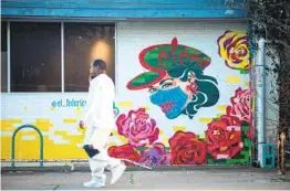  ?? MONTINIQUE MONROE GETTY IMAGES ?? A pedestrian walks past a mural encouragin­g mask wearing in Austin, Texas, on Wednesday. Texas will end its mask mandate on March 10.