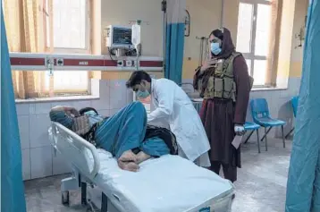  ?? PETROS GIANNAKOUR­IS/AP ?? A doctor looks after a patient Dec. 5 as a member of the Taliban stands behind him in Wazir Mohammad Akbar Khan National Hospital in Kabul, Afghanista­n.