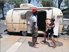  ??  ?? OUTSIDE their 1977 Airstream trailer-turned-barbershop, genderquee­r hairstylis­t Marin Lopez speaks with a client July 17.