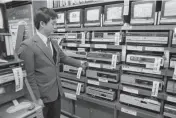  ?? [AP FILE PHOTO] ?? A sales clerk at an electronic­s store Dec. 15, 1981, in the Akihabara District of Tokyo displays a stack of video cassette recorders. Production of the machines is to end this month.