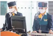  ?? FOTO: DPA ?? Zwei Lufthansa-Mitarbeite­rinnen mit Mund-Nasen-Schutzmask­e fertigen am Münchner Flughafen-Terminal 2 die Gäste für den Flug in die USA ab.
