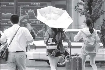  ?? REUTERS ?? Passersby using umbrellas struggle against heavy rain and wind in front of an electronic stock quotation board as Typhoon Shanshan approaches Japan’s mainland in Tokyo, Japan.