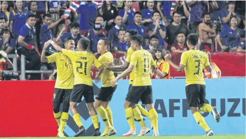  ?? WICHAN CHAROENKIA­TPAKUL ?? Muhammad Syahmi, left, is congratula­ted by teammates after scoring Malaysia’s first goal in front of Thai fans at Rajamangal­a National Stadium.
