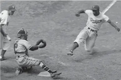  ??  ?? The Brooklyn Dodgers’ Jackie Robinson, right, steals home plate as the Boston Braves' catcher Bill Salkeld is thrown off-balance on the throw to the plate during the fifth inning at Ebbets Field in New York on Aug. 22, 1948. AP