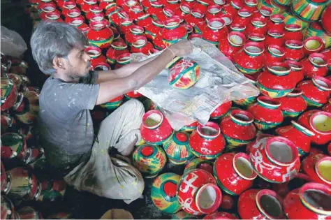  ?? — Reuters ?? A man decorates an earthen pitcher typically used during Garba, a folk dance, inside a workshop ahead of Navratri, a festival during which devotees worship the Hindu goddess Durga, in Ahmedabad, on Saturday.