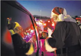  ?? John Locher The Associated Press ?? Charlie Bush, dressed as Santa Claus, wears a face shield as he greets people in their cars at Glittering Lights, the drive-thru holiday display at Las Vegas Motor Speedway.