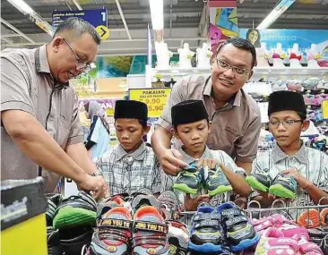  ??  ?? Festive shopping: MAIJ officials Islahudin Jalal (left) and Mohd Abd Jalil Saturi helping (from second left) Afiq, Aziq and Alif choose their shoes at the hypermarke­t in Nusajaya.