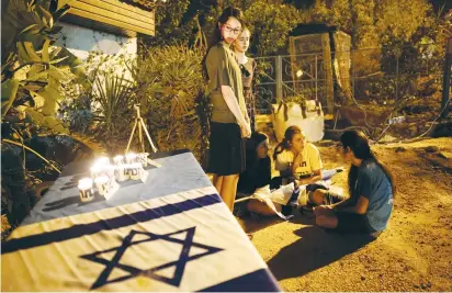  ?? (Amir Cohen/Reuters) ?? YOUTHS GATHER by candles and an Israeli flag placed next to the Salomon family home in Halamish on Saturday night after three members of the family were killed in a terrorist attack.