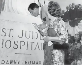  ?? THE COMMERCIAL APPEAL FILES ?? Feb. 4, 1962: Danny Thomas kisses the toe of St. Jude Thaddeus as Mrs. Thomas looks on during the formal opening of St. Jude Children’s Research Hospital. “This is the greatest day of my life,” the television performer observed. “If I should die this minute, I would know why I was born.” Some 9,000 people turned out for the opening.