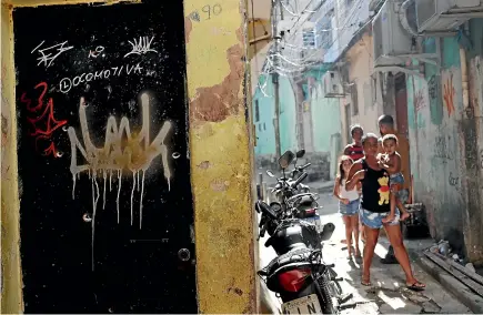  ?? AP ?? Residents walk near a doorway scarred with bullet holes after a police raid against drug trafficker­s in Rio de Janeiro.
