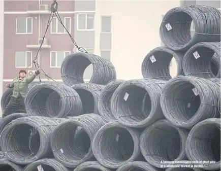  ??  ?? A labourer manoeuvres coils of steel wire at a wholesale market in Beijing.