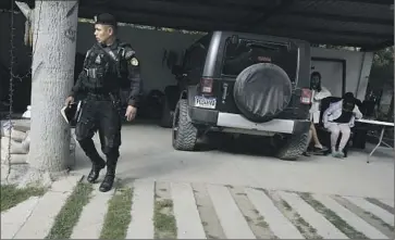  ?? A POLICE OFFICER Moises Castillo Associated Press ?? walks near suspects arrested in a raid in Huehuetena­ngo, Guatemala. Authoritie­s targeted a migrant smuggling ring for which they’ve documented $2 million in revenue since 2019.