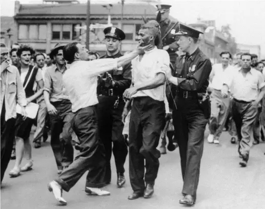  ?? ASSOCIATED PRESS ?? A white man slaps a black man in police custody during Detroit race riots on June 21, 1943.