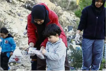  ??  ?? Shameen Rihana helps a Syrian child put on gloves as they collect rubbish as part of her group’s activity, which teaches young refugees about the importance of hygiene.