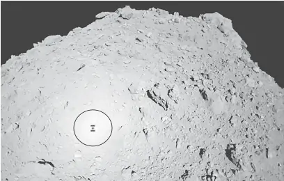  ?? — Gambar AFP ?? MISI BERJAYA: Gambar serahan JAXA diterima daripada pesawat angkasa Hayabusa2 semalam (waktu Jepun) menunjukka­n bayang-bayang Hayabusa2 (dalam bulatan) di atas asteroid Ryugu semasa operasi pengaturan kedudukan MASCOT.