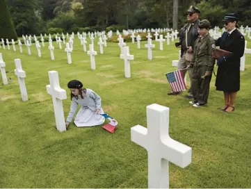  ?? JEREMIAS GONZALES/AP ?? A girl named Alice places a flower by a headstone while members of her family look on Saturday at the Normandy American Cemetery in Colleville-sur-Mer, France. Several ceremonies are scheduled to take place on Monday to mark the 78th anniversar­y of D-Day, which led to the liberation of France and other European countries in World War II.