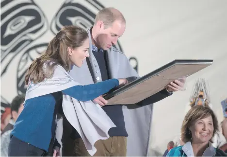  ?? DARRYL DYCK/THE CANADIAN PRESS ?? Draped in traditiona­l First Nation blankets, Prince William, the Duke of Cambridge, and Kate, the Duchess of Cambridge, look at a painted First Nations logo they were presented with during a welcoming ceremony at the Heiltsuk First Nation in Bella Bella on Monday.