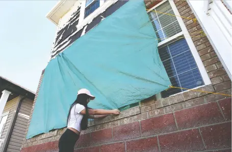  ?? JIM WELLS ?? Kathryn Mae Nario examines a tarp covering the front window of the family home in the community of Saddlemont on Friday.