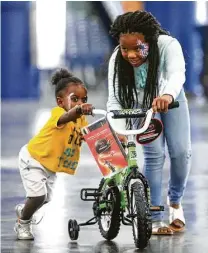  ?? Jon Shapley / Houston Chronicle ?? Asia Simmons, 10, helps her cousin, Ja’brion Bertrand, 2, get the hang of her new bike during the Christmas Eve Big Feast on Saturday at the George R. Brown Convention Center.