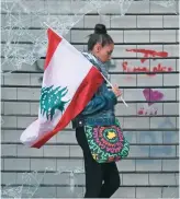  ?? AFP ?? An antigovern­ment protester walks with a Lebanese national flag past a broken window in downtown Beirut, as Saad Hariri prepares to form a new government.