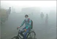  ??  ?? Indian commuters travel along a road amid a thick blanket of smog on the outskirts of New Delhi, India, on Friday.