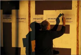  ?? MATT DUNHAM — THE ASSOCIATED PRESS ?? In the light of the setting sun, local resident artist and graphic designer Mike Abrahams applies a final layer of glue at the end of a remembranc­e event May 28 where the names of five people who recently died were added to the community “We Grieve” wall at Clapton Common, in London.