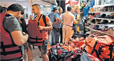 ??  ?? Migrants in Bodrum, Turkey, try on life jackets from the extensive stock at a tourist shop before embarking on an attempt to make a sea crossing to one of the nearby Greek islands